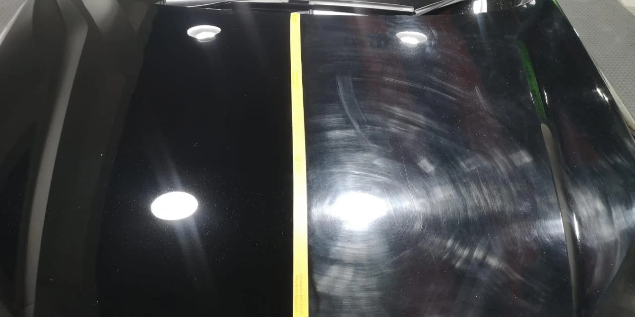A black Honda HR-V bonnet split by a strip of yellow tape: the polished left side reflects the studio lights cleanly, the untouched right side is covered in circular swirl marks